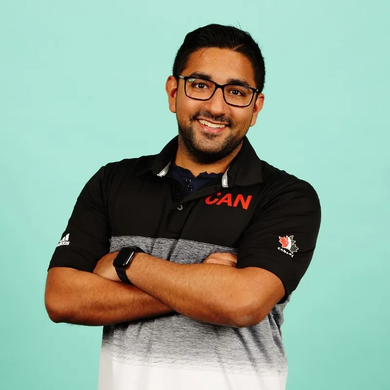 Half body shot of Ajay in a collared greyscale shirt, arms crossed, and smiling towards the camera standing in front of a light blue backdrop.